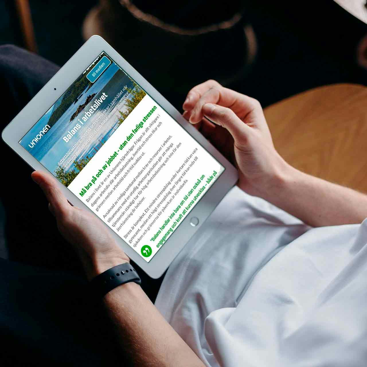 A man sitting on a sofa with an iPad on his lap, browsing Unionen's website.