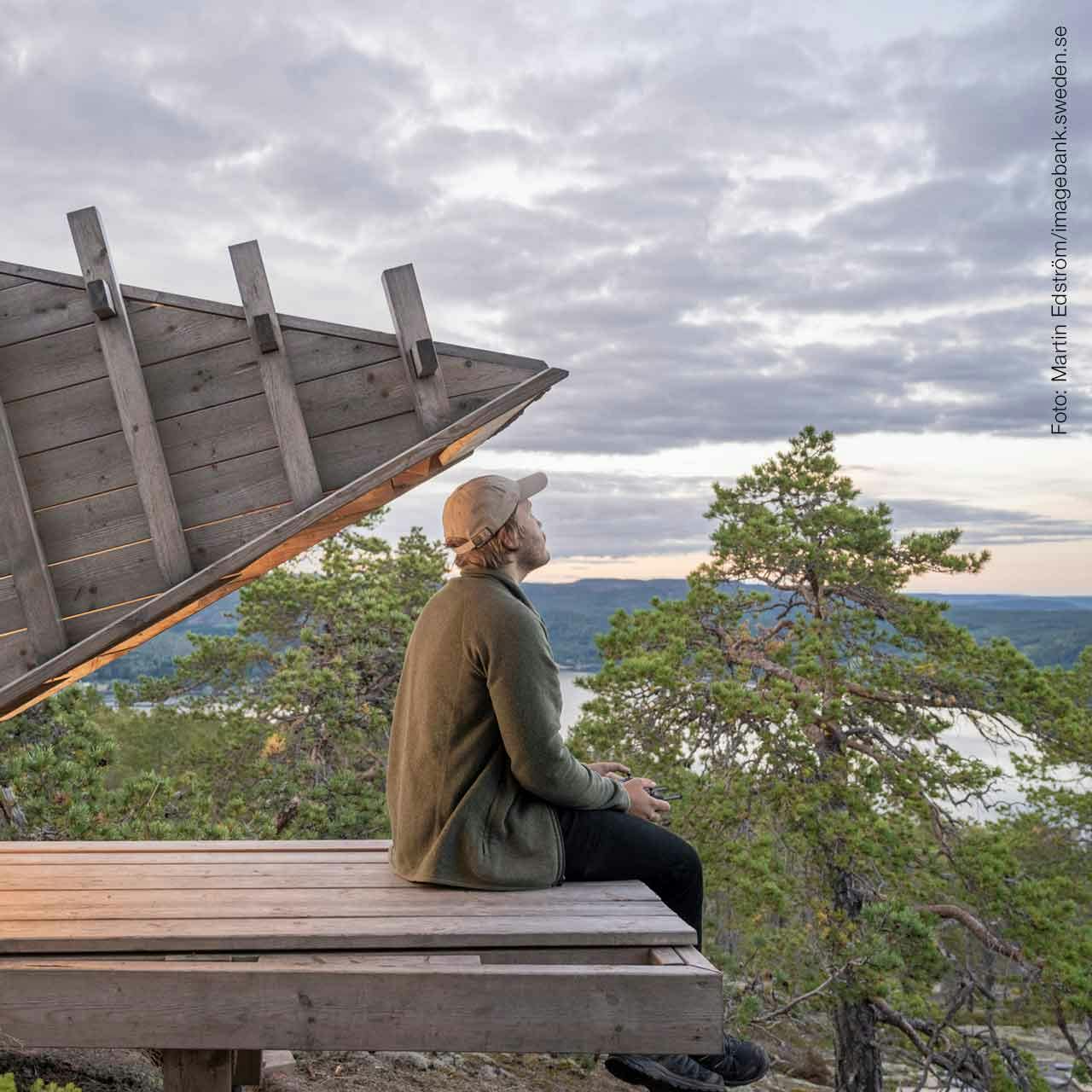 A person sitting on a wooden deck atop a mountain, looking out over the Swedish mountains